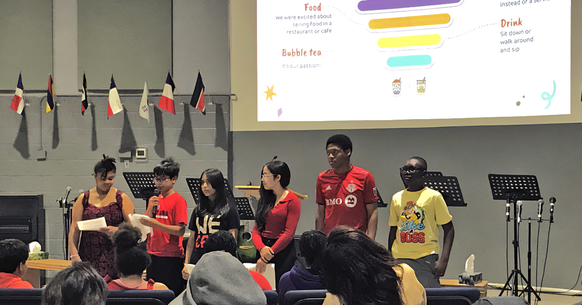 Six young people stand in front of a screen with a powerpoint presentation